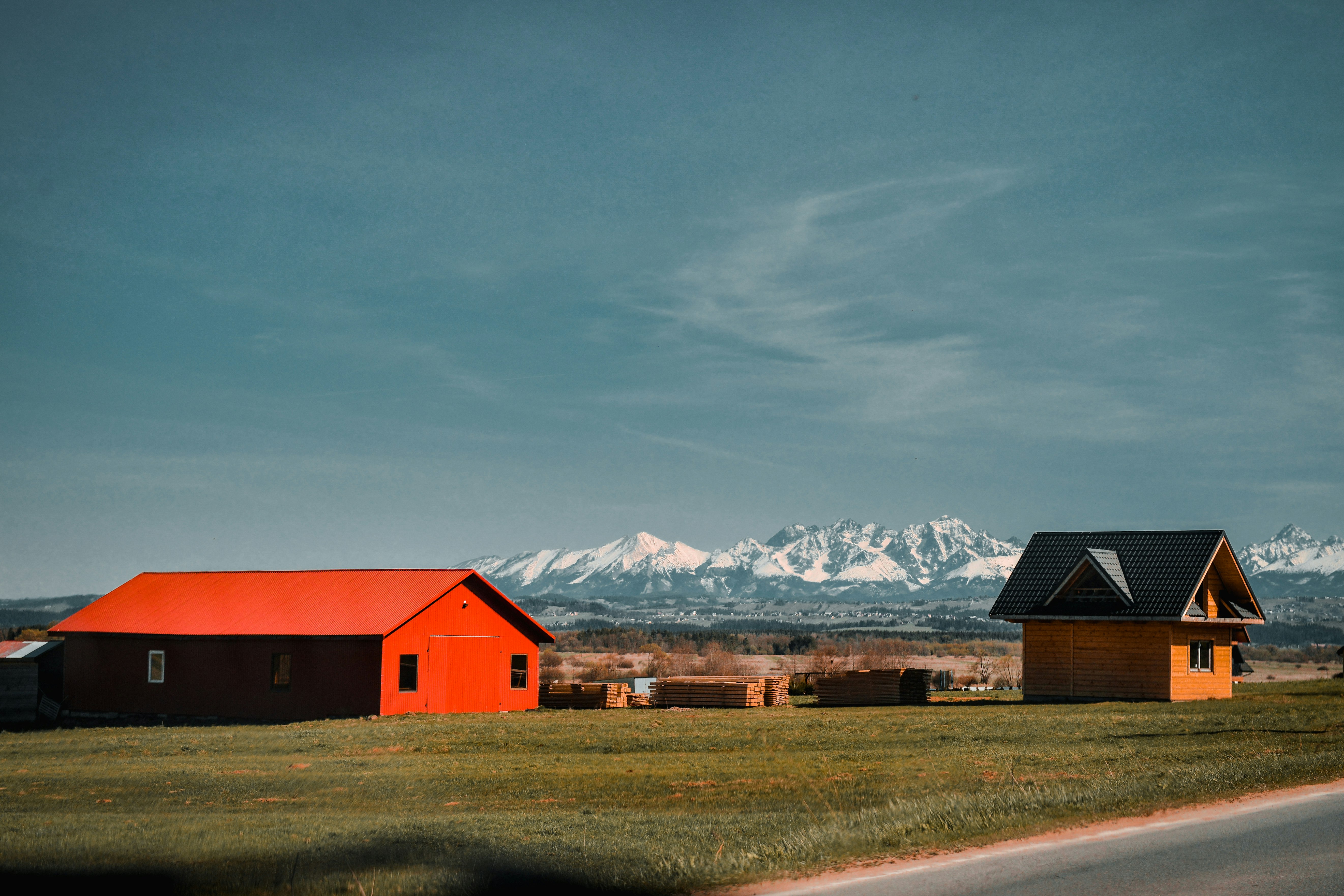 red and black barn near brown grass field and snow covered mountains during daytime